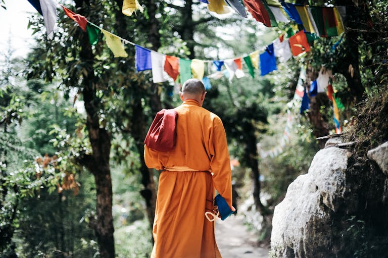 A Buddhist monk walks under colorful prayer flags in a serene forest in Nepal, illustrating spirituality and peace.
