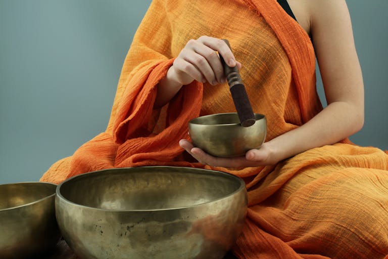 Person in traditional attire using Tibetan singing bowls in a meditative practice.